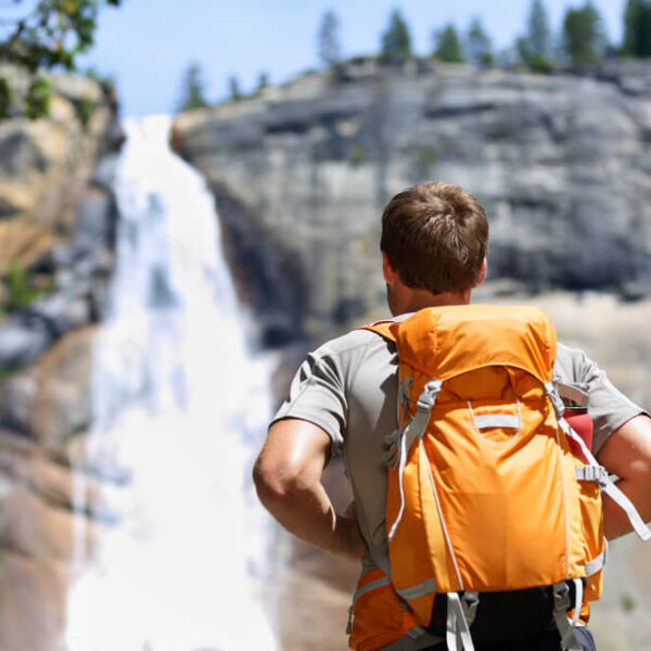 A man with a backpack enjoying the breathtaking beauty of a waterfall.