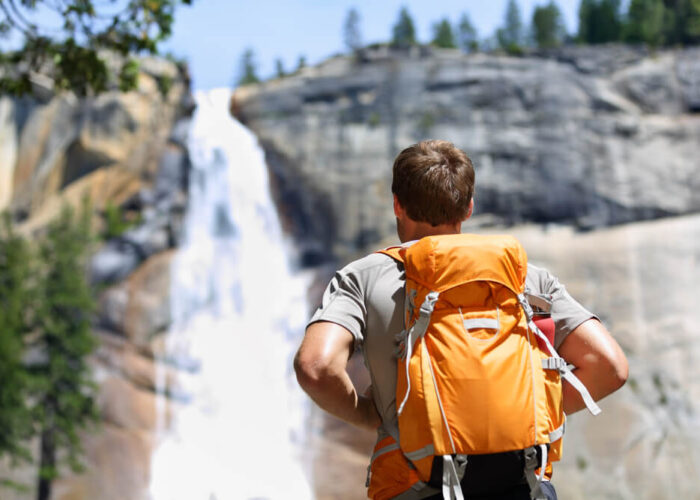 A man with a backpack enjoying the breathtaking beauty of a waterfall.