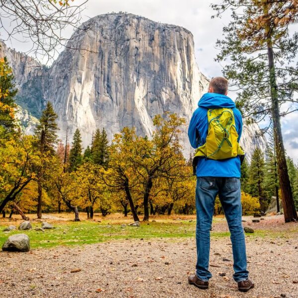 A man is standing in front of a mountain in Yosemite National Park, enjoying one of the stunning tours offered in this magnificent park.