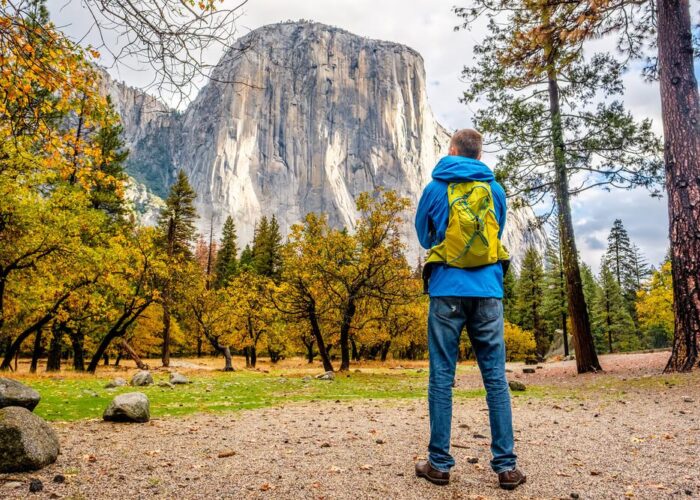 A man is standing in front of a mountain in Yosemite National Park, enjoying one of the stunning tours offered in this magnificent park.