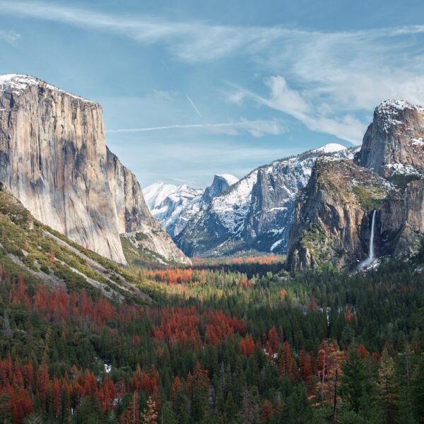 A scenic view of Yosemite Valley with El Capitan on the left, Bridalveil Fall on the right, and Half Dome in the distance, surrounded by forested slopes and dusted with snow