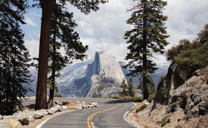 A winding road leading towards a prominent mountain peak with clouds above, inviting visitors on a captivating 3-day Yosemite Escape.