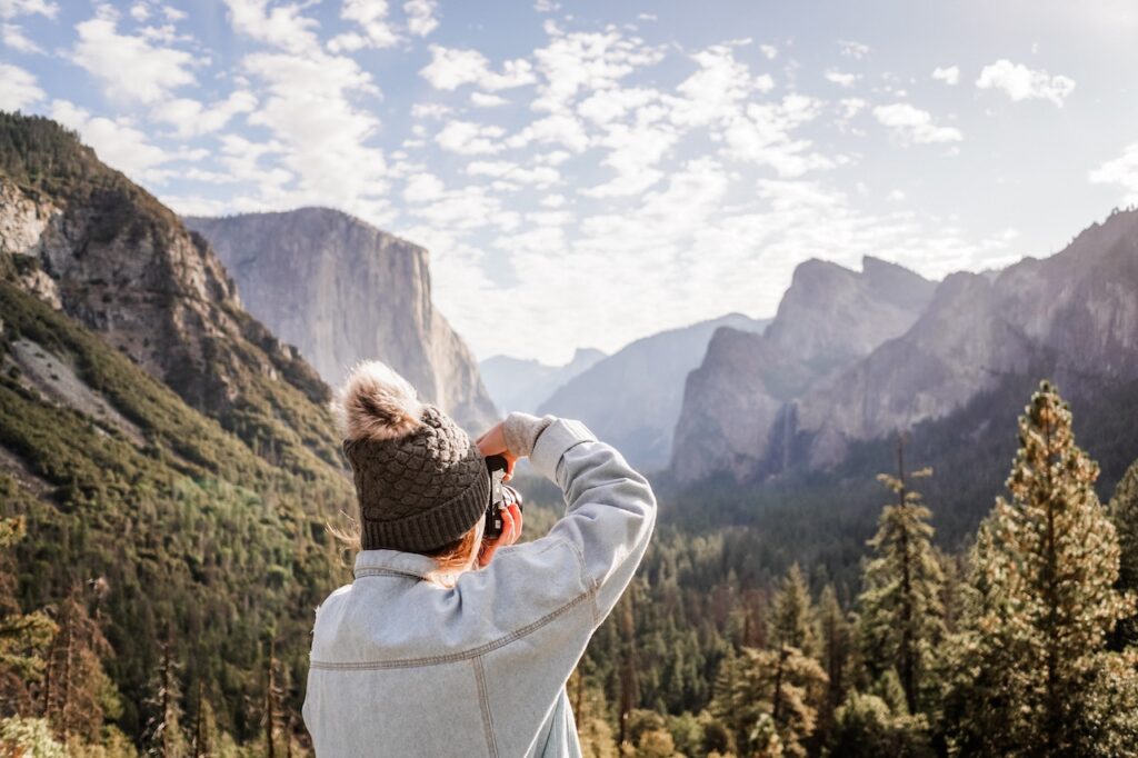 Person in a warm hat capturing a scenic mountain view on a Yosemite Escape Lodging Tour.