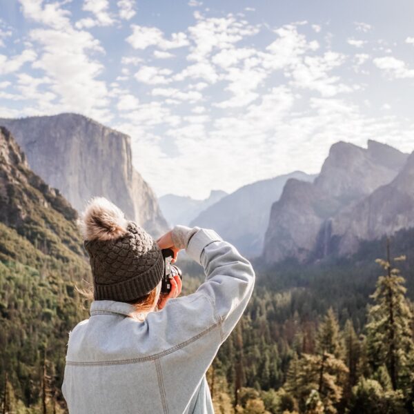 Person in a warm hat capturing a scenic mountain view on a Yosemite Escape Lodging Tour.