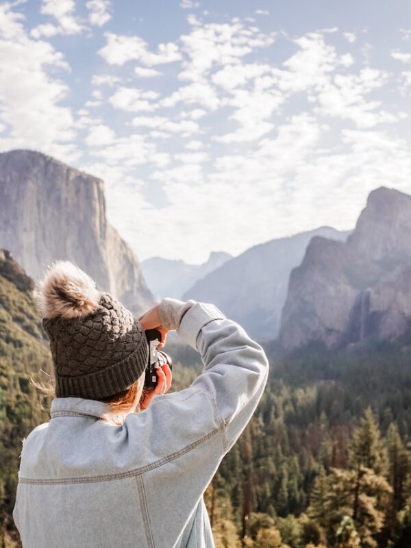 Person in a warm hat capturing a scenic mountain view on a Yosemite Escape Lodging Tour.