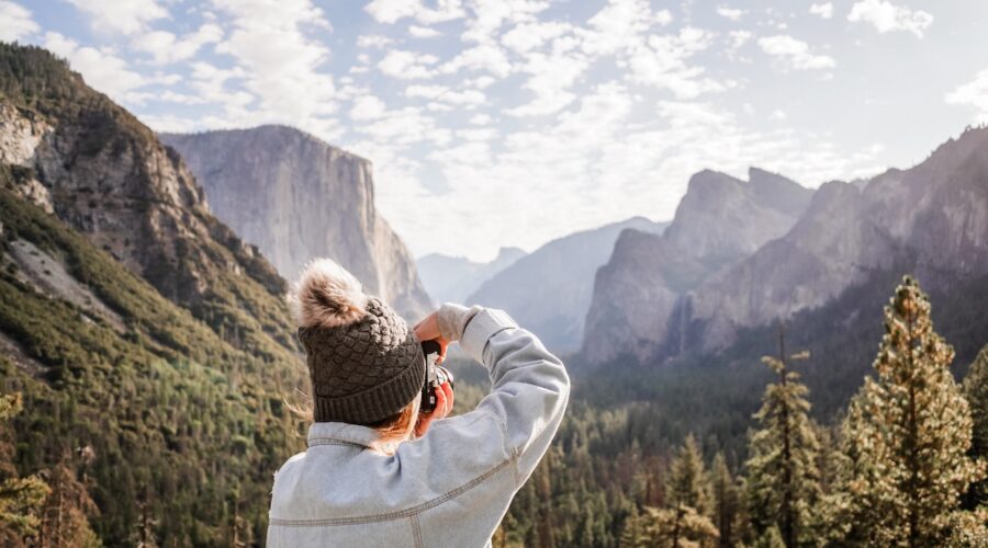 Person in a warm hat capturing a scenic mountain view on a Yosemite Escape Lodging Tour.