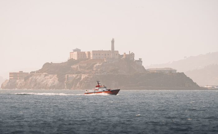 A boat sails near Alcatraz Island on a hazy day, offering tours to Muir Woods and Sausalito.