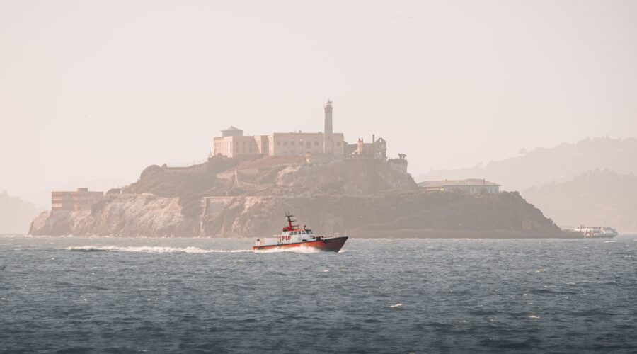 A boat sails near Alcatraz Island on a hazy day, offering tours to Muir Woods and Sausalito.