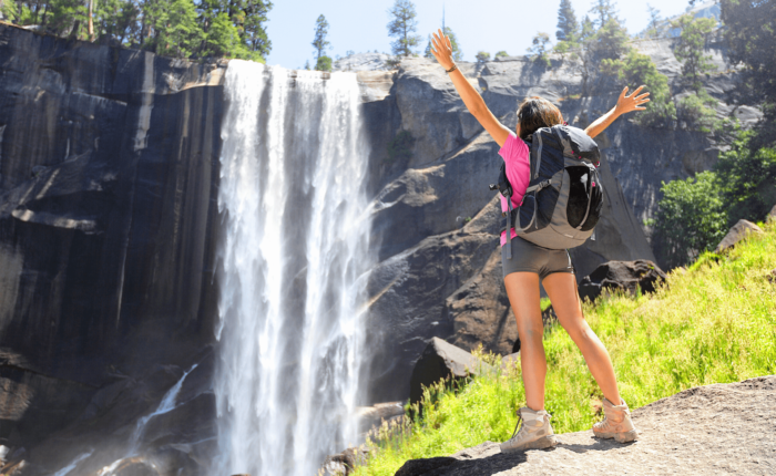 A woman standing in front of a waterfall in Yosemite National Park, California.