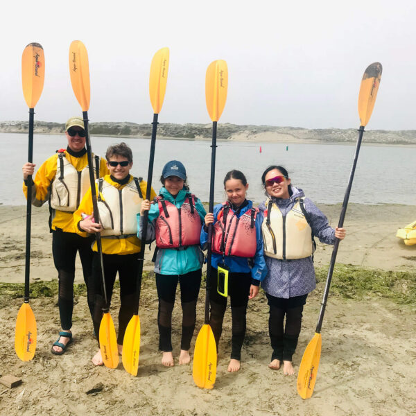 A small group of people posing for a photo with kayaks in California.