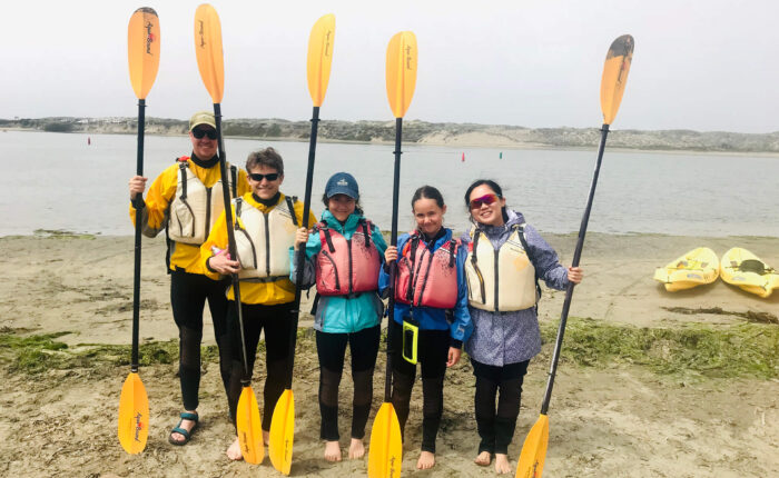 A small group of people posing for a photo with kayaks in California.