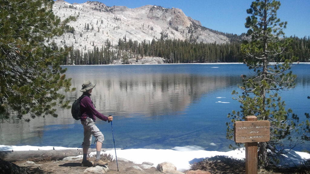 A hiker standing next to a lake in Yosemite National Park with mountains in the background.