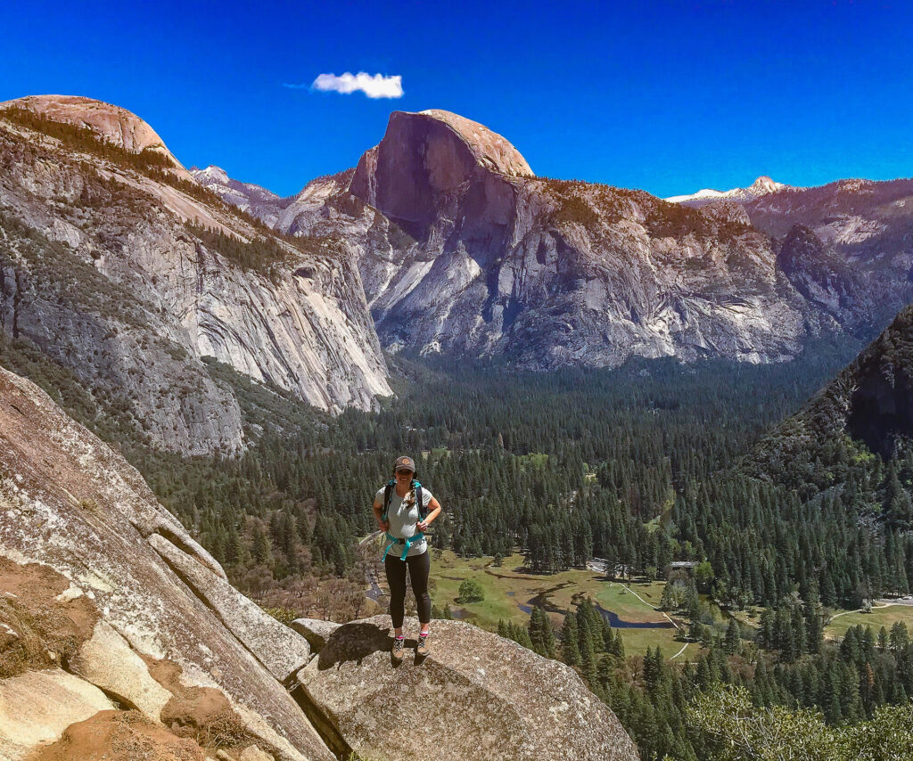 A woman standing on top of a cliff overlooking Yosemite Valley while on a tour from San Francisco.