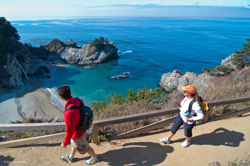 Two people walking on a trail near the ocean in California.