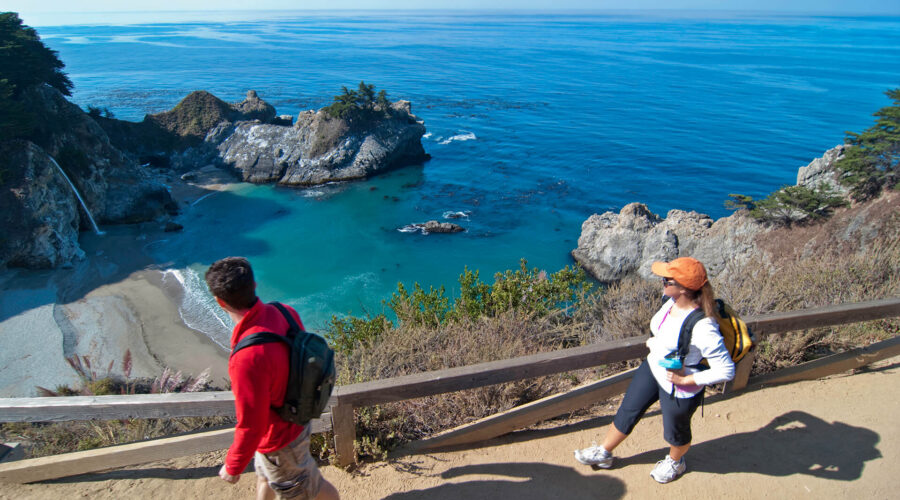Two people walking on a trail near the ocean in California.