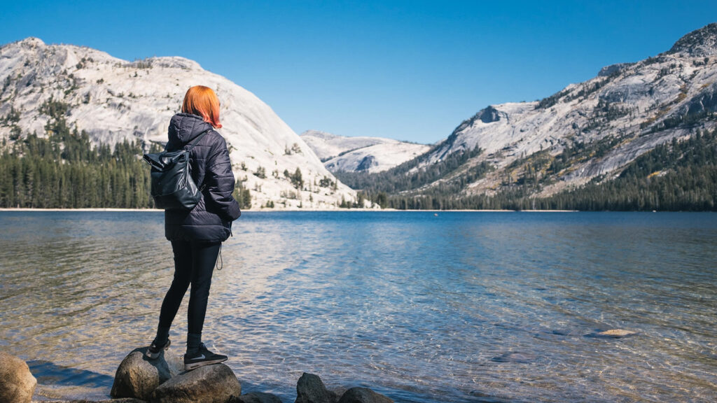 A woman standing on rocks near a lake in Yosemite National Park during a small group tour.