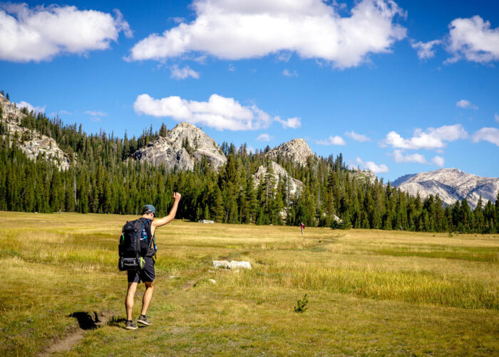 A man in a backpack is walking through a meadow with mountains in the background during a small group tour in California.