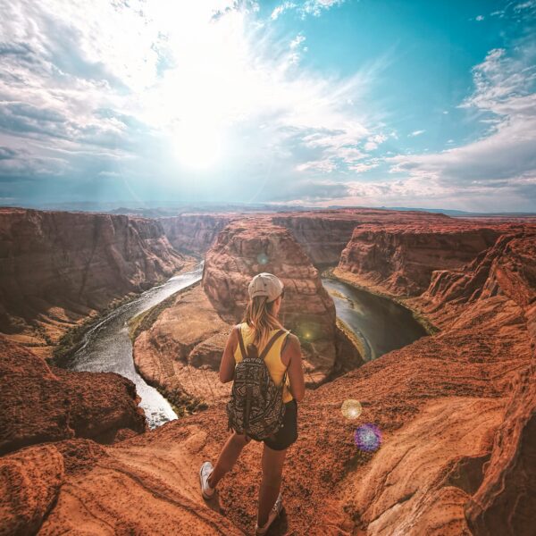 Woman with backpack stands on rocky overlook admiring a Horseshoe Bend