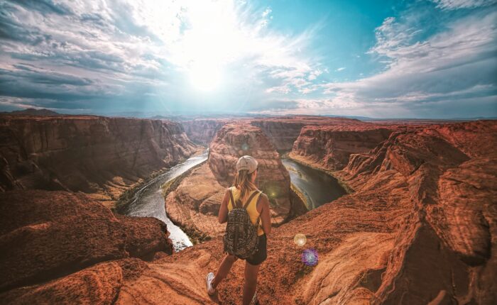 Woman with backpack stands on rocky overlook admiring a Horseshoe Bend