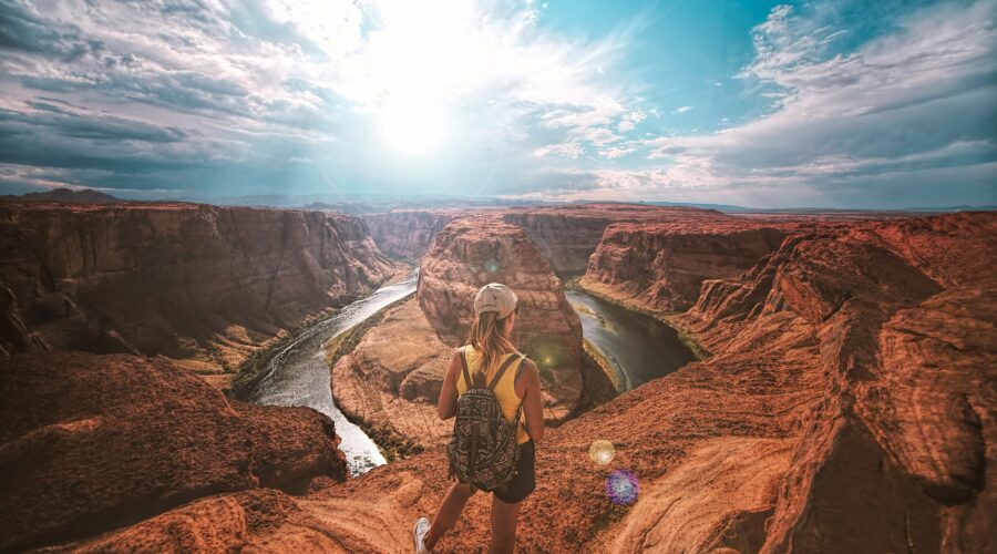 Woman with backpack stands on rocky overlook admiring a Horseshoe Bend