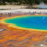Tourists walking along the boardwalk near the vibrant, multicolored grand prismatic spring in Yellowstone National Park