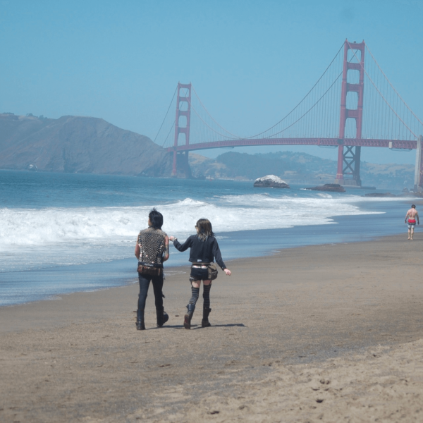Two people walking on a beach near the Golden Gate Bridge in California.