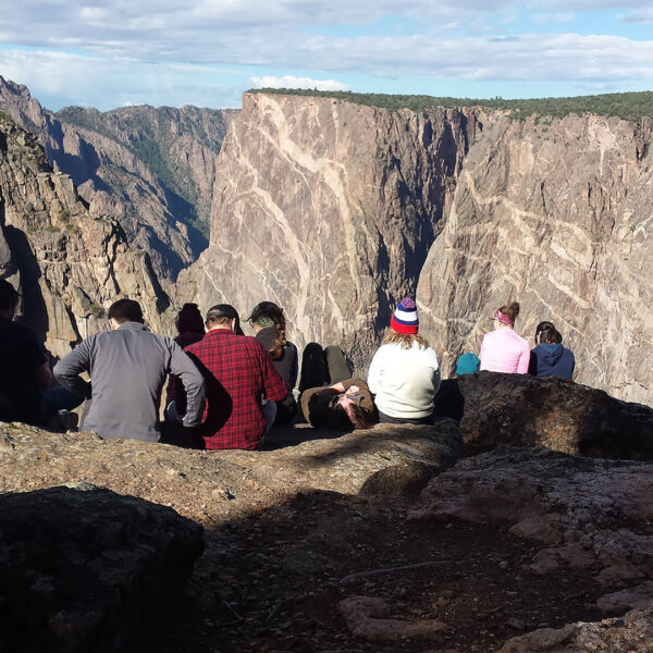 A group of people standing on a cliff overlooking a canyon.