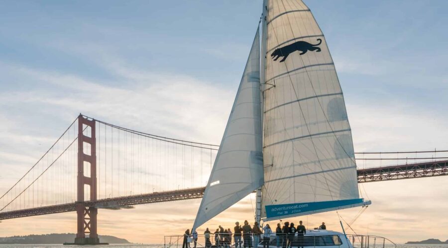 Sailboat with passengers cruising near the golden gate bridge at sunset on a San Francisco Bay sailing tour.