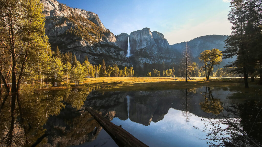 A serene landscape in Yosemite National Park, with a waterfall, cliff face, and trees reflected in a still body of water at dawn or dusk, is good for non-hikers.
