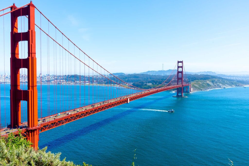 A panoramic view of the Golden Gate Bridge spanning across the bay with a clear blue sky and cityscape in the background.