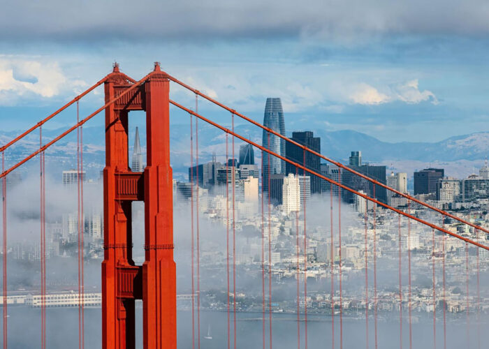 A close-up of the Golden Gate Bridge with the San Francisco skyline and mountains in the background, partially obscured by clouds, captures one of the most iconic US cities in all its scenic splendor.