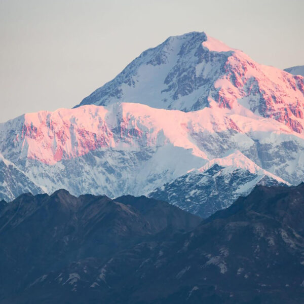 Snow-covered mountain peaks with a pink hue at sunset, set against a clear sky.