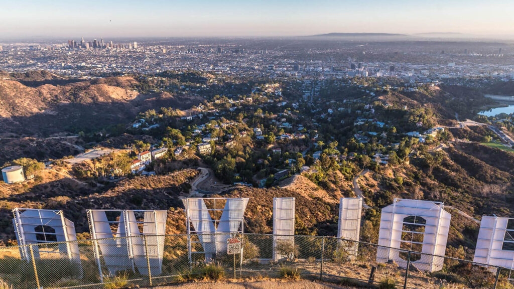 View from behind the iconic Hollywood Sign overlooking the sprawling cityscape of Los Angeles with downtown skyscrapers visible in the distance.