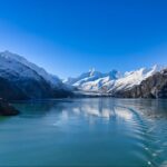 A serene glacier valley with clear blue water, surrounded by snow-capped mountains under a bright blue sky, offers the perfect backdrop for an unforgettable Alaska travel experience. Imagine exploring this breathtaking landscape where the essence of Denali meets the allure of Kenai Fjords.