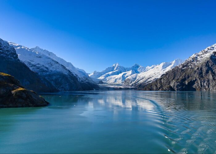 A serene glacier valley with clear blue water, surrounded by snow-capped mountains under a bright blue sky, offers the perfect backdrop for an unforgettable Alaska travel experience. Imagine exploring this breathtaking landscape where the essence of Denali meets the allure of Kenai Fjords.