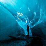 A person stands inside an ice cave at Matanuska Glacier, surrounded by smooth, glowing blue walls, casting a silhouette against the illuminated background—a mesmerizing highlight of the summer tour.