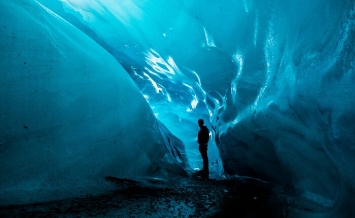 A person stands inside an ice cave at Matanuska Glacier, surrounded by smooth, glowing blue walls, casting a silhouette against the illuminated background—a mesmerizing highlight of the summer tour.