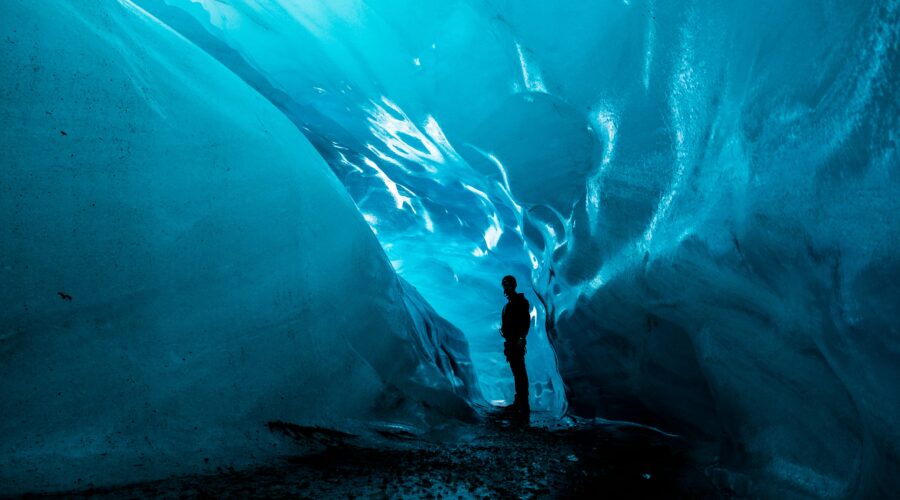 A person stands inside an ice cave at Matanuska Glacier, surrounded by smooth, glowing blue walls, casting a silhouette against the illuminated background—a mesmerizing highlight of the summer tour.