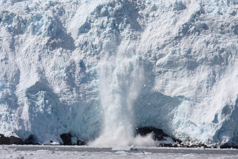 A glacier calving in Kenai Fjords, releasing ice into the sea with water splashing upon impact, offers a breathtaking spectacle for those on an Alaska Cruise.