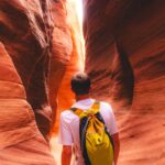 A person with a yellow backpack ambled through a narrow, winding sandstone canyon