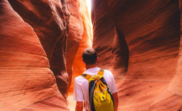 A person with a yellow backpack ambled through a narrow, winding sandstone canyon