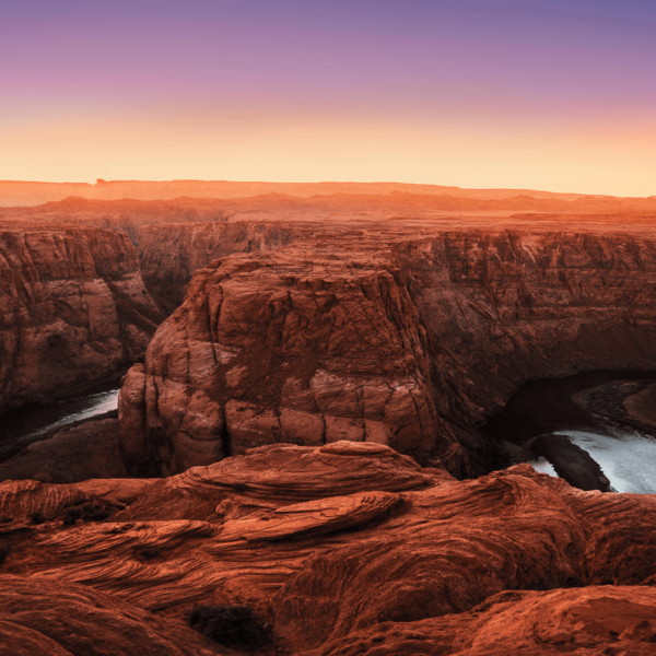 Aerial view of a winding river cutting through rugged red rock canyons at sunset.