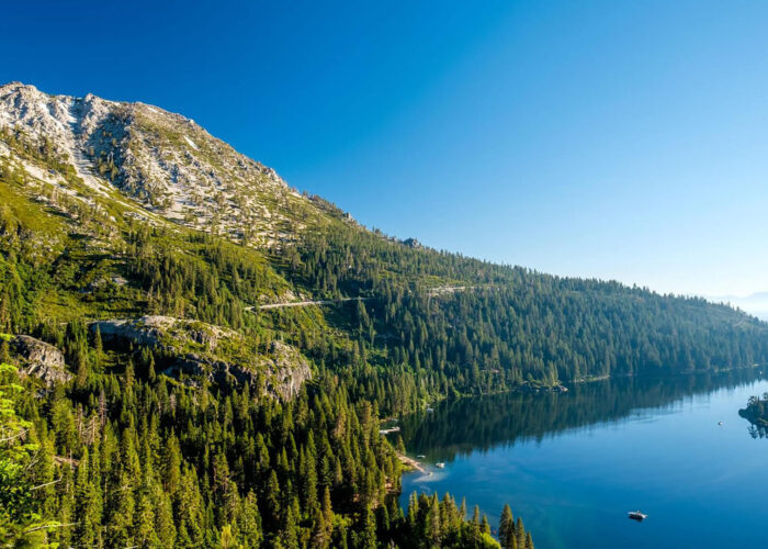 Nestled within Yosemite's grandeur, a clear blue lake reflects the bright sky, bordered by dense green forests and rugged mountains—a perfect nature getaway.