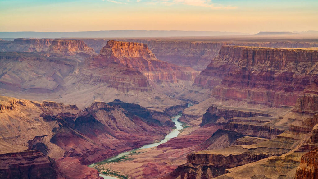 Wide view of the Grand Canyon at sunset, showcasing layered rock formations, cliffs, and a river winding through the canyon floor—one of the best travel style experiences near West Coast National Park.