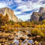 A river with rocks flows through a Yosemite valley surrounded by tall cliffs, pine trees, and autumn foliage—a magical escape under a partly cloudy November sky.
