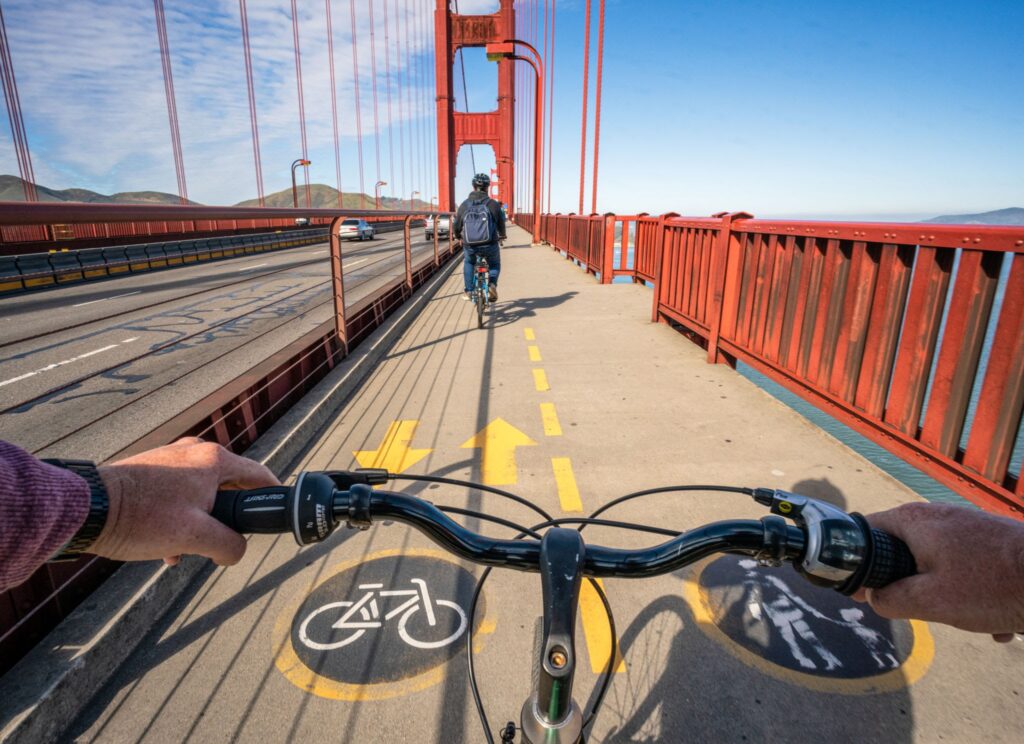 Experience a cyclist’s view riding across the Golden Gate Bridge on a sunny day, following another rider in the bike lane—just one adventure featured in our San Francisco Neighborhood Guide.