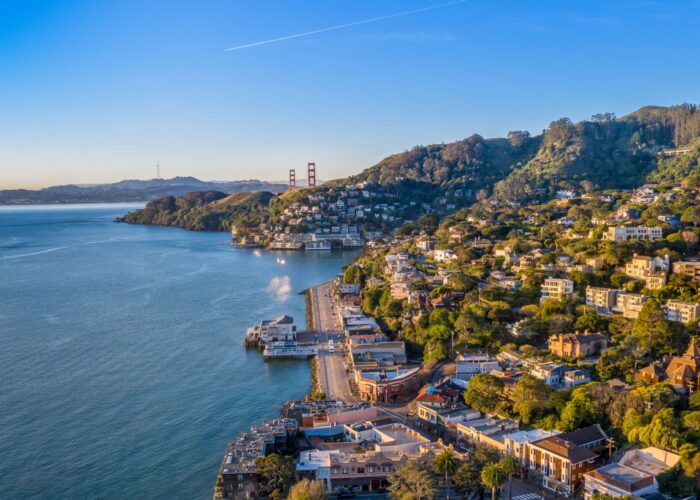 Aerial view of a Sausalito with hillside houses, a waterfront road, and the Golden Gate Bridge in the background under a clear blue sky—perfect for any San Francisco Neighborhood Guide.